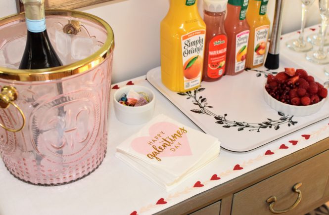 Galentines mimosa bar with juice, glasses, a heart table runner and champagne